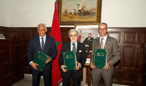 Nouveau-projet205 | MCG24 | موقع إلكتروني مغربي شامل متجدد على مدار الساعة Three men in suits stand side by side, each holding a green folder during an official ceremony, with a Moroccan flag behind them.
