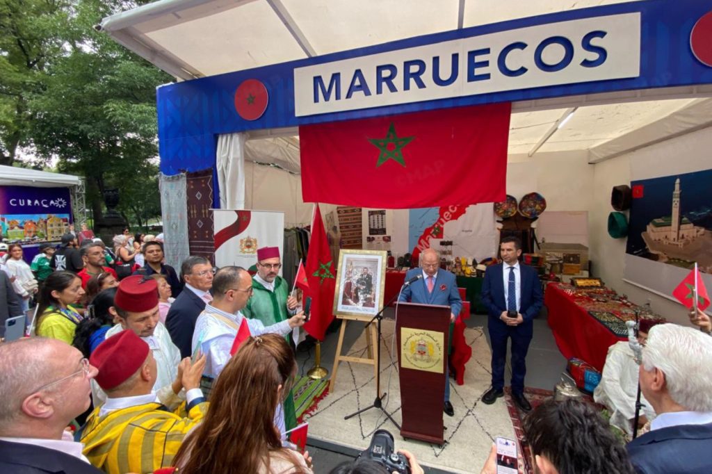 Morocco booth at a cultural festival with a red Moroccan flag and a speaker at a podium addressing a crowd