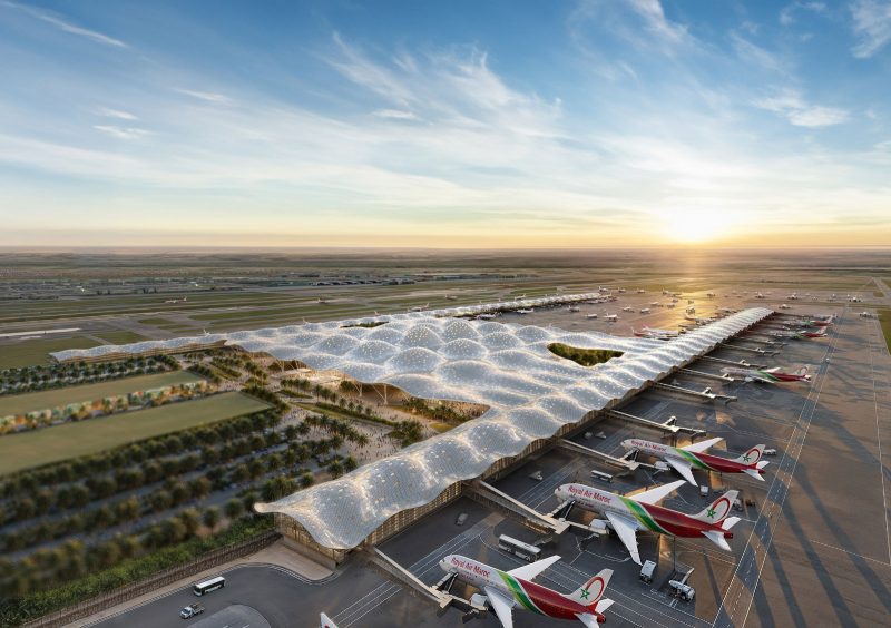 WhatsApp-Image-2025-03-20-at-104003 | MCG24 | موقع إلكتروني مغربي شامل متجدد على مدار الساعة Sunset at a modern airport with a wavy, perforated roof over the gates and numerous parked airplanes lined up at the jetways