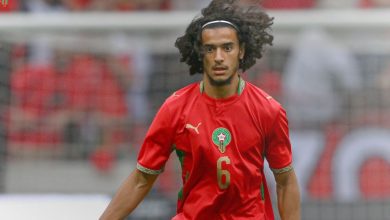 Soccer player with curly hair in a red Morocco-style jersey, number 6, on the field during play.