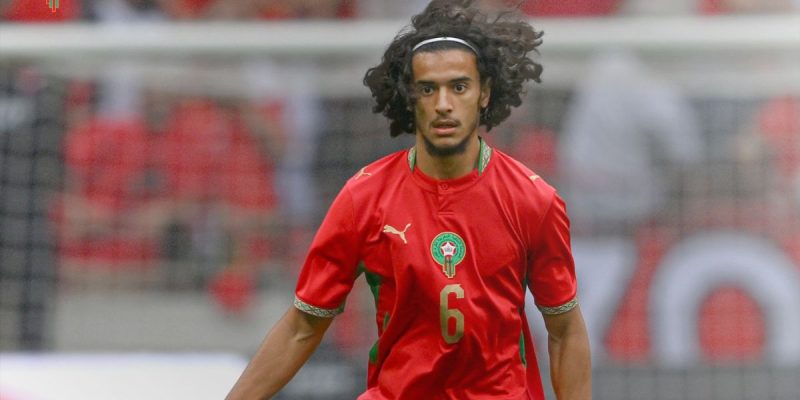 Soccer player with curly hair in a red Morocco-style jersey, number 6, on the field during play.