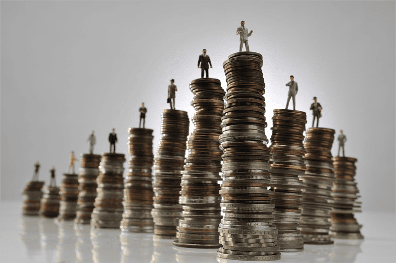 fortune-plus-riches | MCG24 | موقع إلكتروني مغربي شامل متجدد على مدار الساعة Miniature businesspeople stand on stacked coins of varying heights, illustrating the financial ladder and progression.