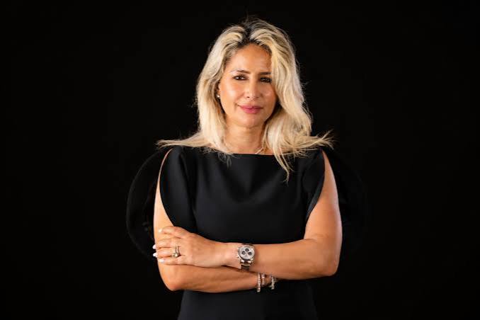 images | MCG24 | موقع إلكتروني مغربي شامل متجدد على مدار الساعة Professional woman with blonde hair in a black dress, arms crossed, against a dark background.