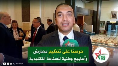 Male reporter in a suit speaks to camera in a lobby; green Arabic caption mentions organizing exhibitions and national weeks for traditional crafts.