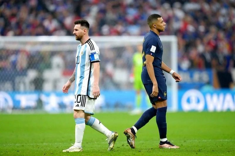 messi-mbappe | MCG24 | موقع إلكتروني مغربي شامل متجدد على مدار الساعة Two soccer players walk on the field during a match, one in a light blue-and-white striped jersey and the other in a dark blue kit, with a blurred crowd in the background.
