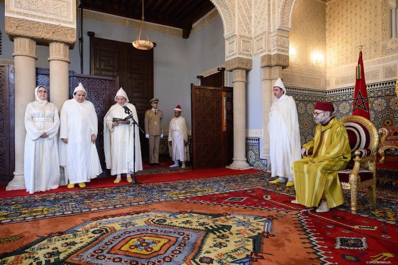 mohammed-VI-recoit-a-Rabat-plusieurs-ambassadeurs-etrangers13 | MCG24 | موقع إلكتروني مغربي شامل متجدد على مدار الساعة Moroccan king in yellow robes sits on a throne in a richly decorated hall, with officials standing and guards nearby.