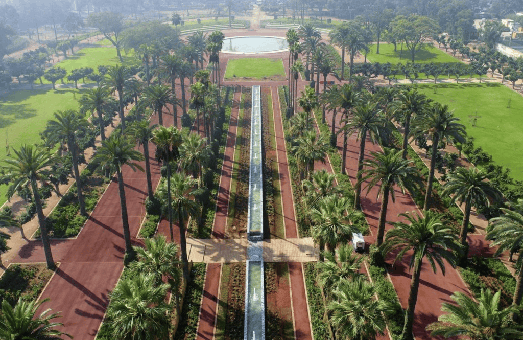 screenshot-2026-06-18-123636 | MCG24 | موقع إلكتروني مغربي شامل متجدد على مدار الساعة Aerial view of a formal park with red brick paths, tall palm trees, and a central long fountain leading to a circular pond.