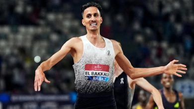 vis_0601202600241904 | MCG24 | موقع إلكتروني مغربي شامل متجدد على مدار الساعة Male sprinter in a white-to-gray sleeveless top with bib El Bakkali Rabat, arms outstretched in celebration on a track.
