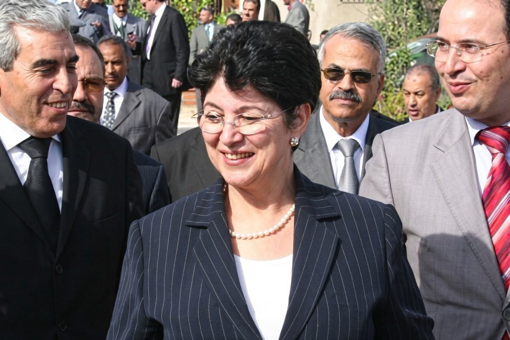 الوزيرة السابقة لطيفة العابدة | MCG24 | موقع إلكتروني مغربي شامل متجدد على مدار الساعة Smiling woman in a navy pinstripe suit and pearl necklace, flanked by men in suits at an outdoor formal event.