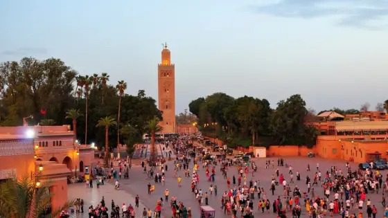مدينة-مراكش-تسجل-رقمًا-قياسيًا-تاريخيًا-في-السياحة | MCG24 | موقع إلكتروني مغربي شامل متجدد على مدار الساعة Crowded plaza in Marrakech with the Koutoubia minaret, palm trees, and warm sunset light.