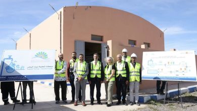 Group of workers and engineers in high‑visibility vests pose in front of a water treatment facility with informational boards beside them.