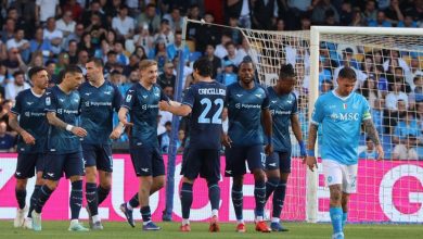 Soccer players in dark blue jerseys celebrate near the goal as teammates congratulate each other, with a light-blue-clad goalkeeper walking away in the foreground.