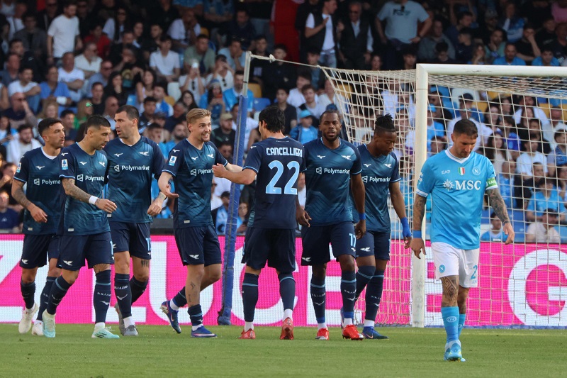 Soccer players in dark blue jerseys celebrate near the goal as teammates congratulate each other, with a light-blue-clad goalkeeper walking away in the foreground.