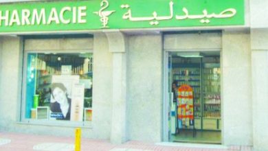 Pharmacy storefront with green sign displaying 'PHARMACIE' and Arabic text, open entrance showing shelves inside.