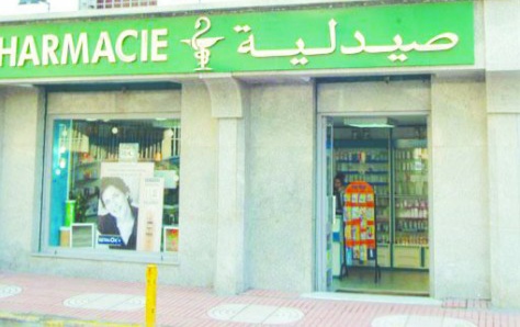 Pharmacy storefront with green sign displaying 'PHARMACIE' and Arabic text, open entrance showing shelves inside.