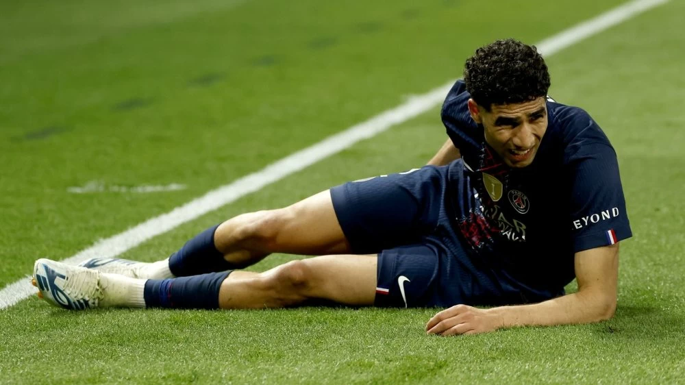 Soccer player in a dark kit lying on the grass, appearing injured near the sideline.