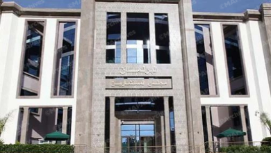 Front view of a modern building entrance with tall stone pillars and glass doors; Arabic sign above the doorway.