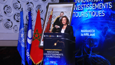 Speaker at a conference podium on innovation and tourism investments, flanked by Moroccan flags, with a blue Marrakech 24 April 2026 banner in the background.