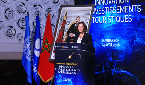 Speaker at a conference podium on innovation and tourism investments, flanked by Moroccan flags, with a blue Marrakech 24 April 2026 banner in the background.