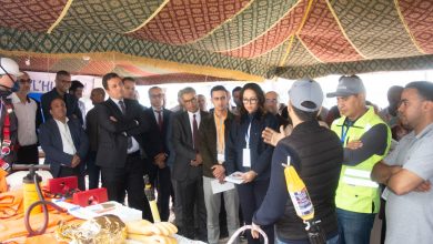 A group of professionals in a tent, listening to a demonstration by a presenter showing safety equipment laid out on a table, including hoses, gloves, and helmets.