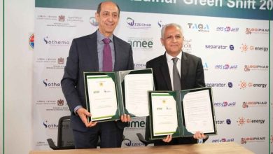 Two men in suits hold framed certificates during a signing ceremony in front of a branded backdrop.