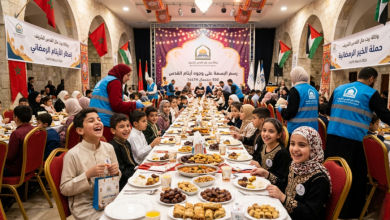 Children and adults sit along a long banquet table enjoying Ramadan iftar, with plates of pastries and drinks in a festively decorated hall.