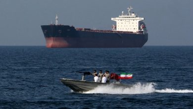 Large cargo ship on the horizon as a speedboat with five men and an Iranian flag speeds across the sea.