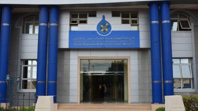 Front façade of a blue-columned public building with a glass entrance and a blue sign above the door written in Arabic and French style text.