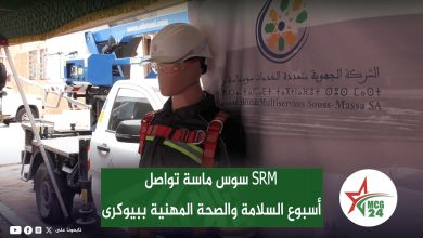 Mannequin wearing a hard hat and safety harness in front of a banner for occupational safety week, with a truck-mounted lift in the background and an MCG 24 logo on the right.