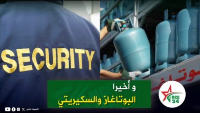 Security guard with a blue jacket labeled SECURITY standing beside a rack of blue gas cylinders; green Arabic banner across the bottom and a round MCG24 logo on the right.