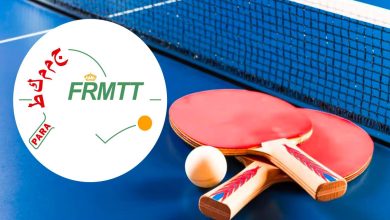 Paddles and ball on a blue table with a net, plus a white circular FRMTT logo overlay.