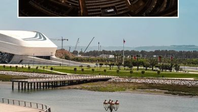 Exterior view of a waterfront park with a futuristic white building and boardwalk, and an inset showing a geometric-lit auditorium interior.