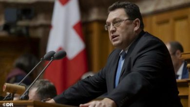 Man in a suit speaking at a wooden podium in a formal government chamber with a Georgian flag behind him.