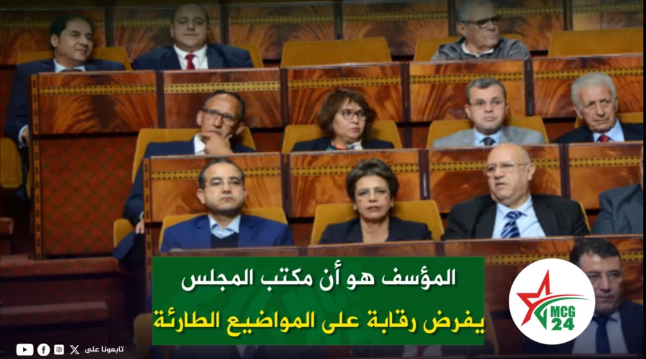 Group of officials seated in a parliamentary chamber; a green banner with Arabic text and a circular logo in the foreground on the right.