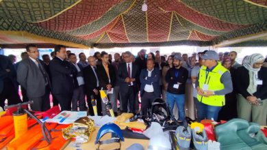 Group of professionals under a decorative canopy watching a display of safety gear on tables (helmets, life jackets, vests).