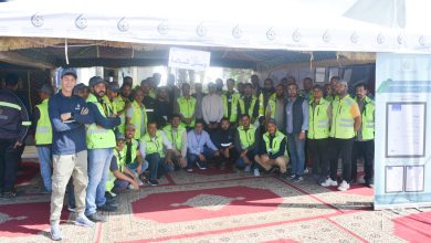 Group of workers wearing neon safety vests posing under a white canopy at an outdoor event.