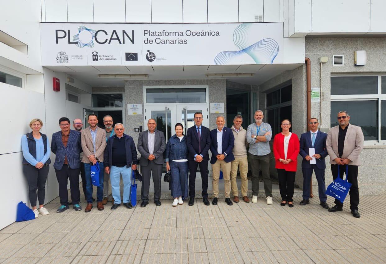 Group of professionals standing in a line outside the PLOCAN facility in the Canary Islands, posing for a photo. Signage above reads Plataforma Oceanica de Canarias (PLOCAN).