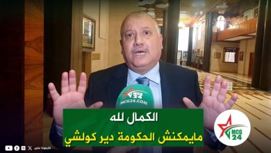 Man in a suit giving an interview in a marble lobby, hands raised, with a green Arabic caption and MCG24 microphone in front of him.