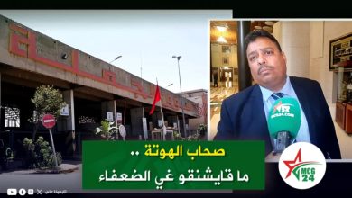 Split-screen video thumbnail: left side shows a concrete public building with red signage and a flag; right side shows a man in a suit being interviewed with a green microphone, overlaid by a green caption banner with Arabic text.