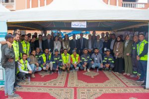 Group photo of workers and officials under a tent at an outdoor safety event, many wearing neon vests and badges.