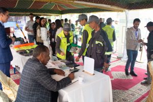 Registration desk at an outdoor safety expo; a man signs papers while attendees in reflective vests browse brochures under a tent