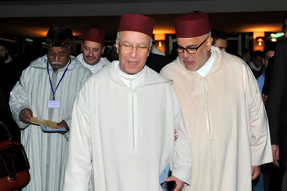 Three men in white robes and red fezzes walk together at an indoor event; the man in the center smiles while holding a booklet.