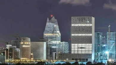 Night city skyline with illuminated modern buildings, including a pyramid-like glass tower and a tall rectangular office block.