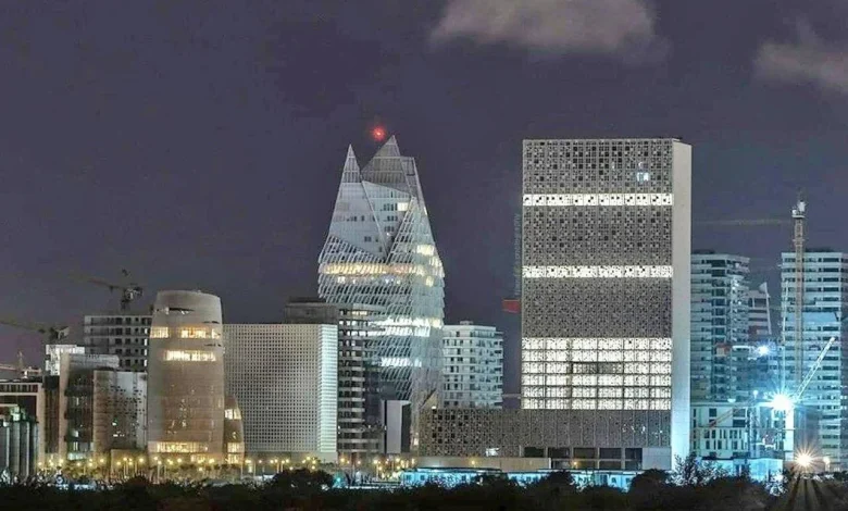 Night city skyline with illuminated modern buildings, including a pyramid-like glass tower and a tall rectangular office block.