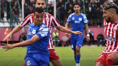Soccer players in blue and red striped kits compete for the ball on a green field during a match at midfield moment.