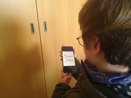 Person seen from behind, wearing a scarf, holding a smartphone showing a drawing on the screen near a wooden cabinet