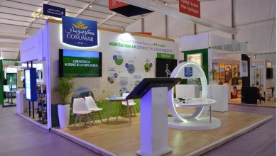 COSUMAR exhibition booth featuring a large blue logo sign, a circular white display ring, and a wall exhibit about Agriculture 4.0 on a wooden platform.”,