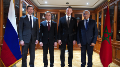 Four officials in suits stand for a formal meeting between Russia and Morocco, with flags on either side.
