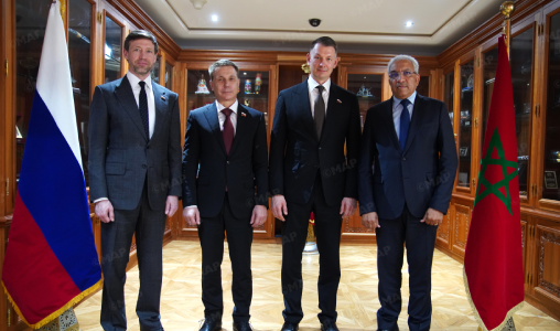 Four officials in suits stand for a formal meeting between Russia and Morocco, with flags on either side.