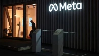 Night view of the Meta office entrance with the glowing Meta logo on a dark exterior and a person entering through glass doors.